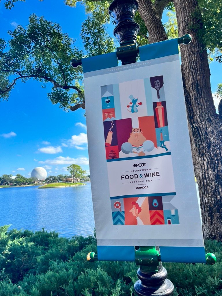 Picture of EPCOT's International Food and Wine Banner with the lake and Spaceship Earth in the background