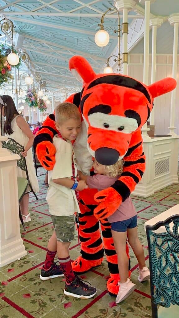 Two children sharing a magical hug with Tigger during a character dining experience at Walt Disney World’s Crystal Palace restaurant, capturing the joy and special moments only Disney can offer.