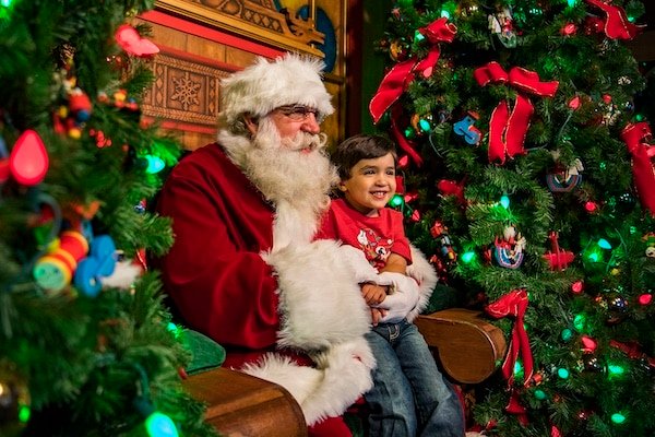 Disney's professional shot of Santa Clause during the holidays at Walt Disney World while holding a young boy and surrounded by garland and other holiday decorations.