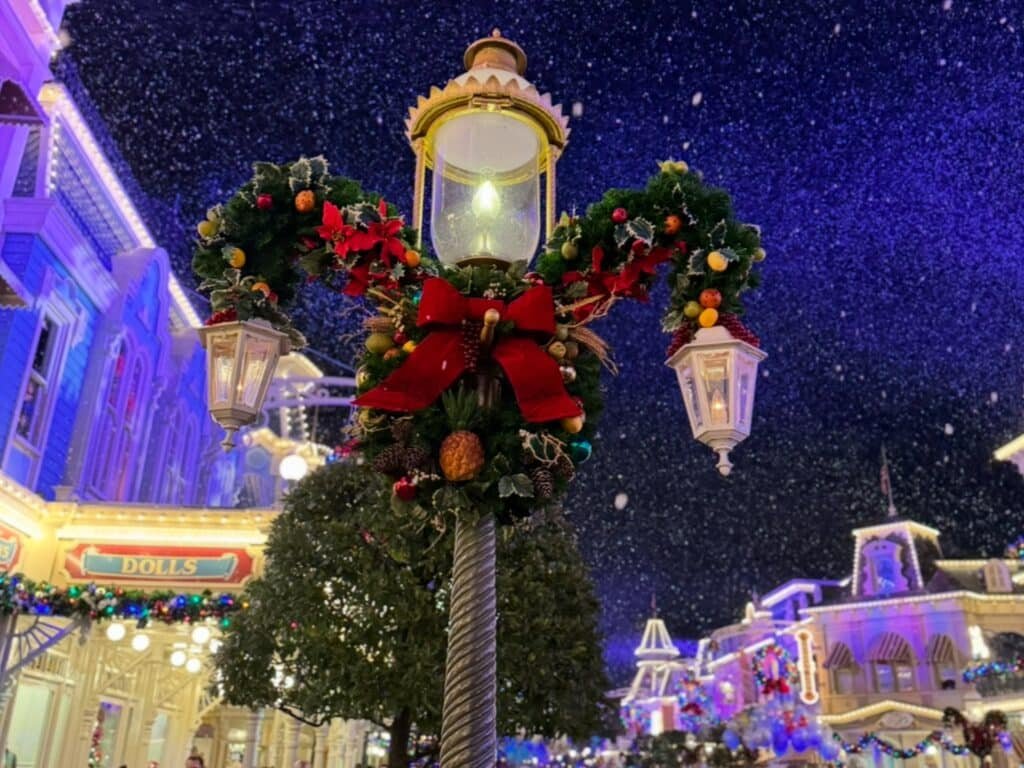 Magic Kingdom Lightpost with a wreathe on it for the holidays. Snow is falling in the background.