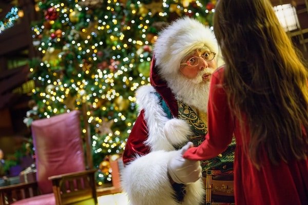 Image of Santa with a little girl during a meet and greet in Disneyland with a Christmas tree lit up in the background.