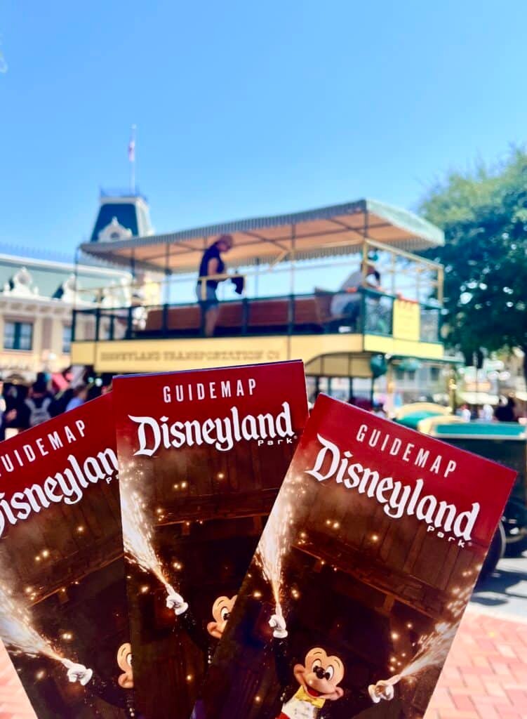 3 Disneyland Park Guide maps and a double decker trolley on Mainstreet U.S.A. in Disneyland Park on a clear blue sky day