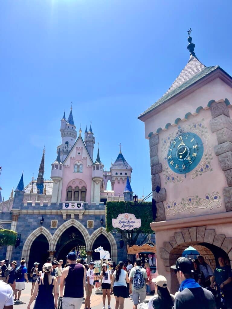 Back of the Sleeping Beauty Castle and Bippity Boppity Boutique Sign with crowds on a clear, blue-sky day