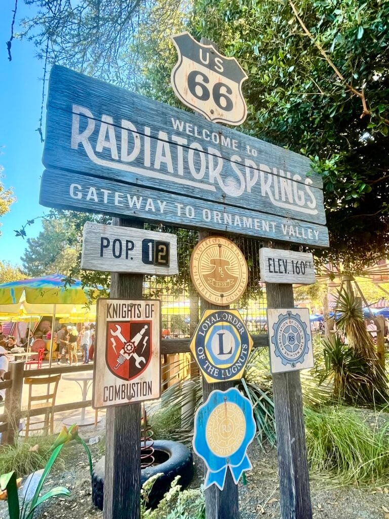 Welcome To Radiator Springs Sign with multiple street signs below the main sign and a Route 66 sign above.