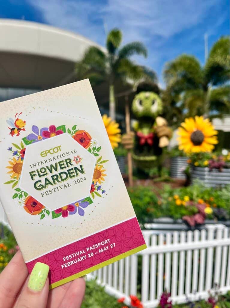 2024 EPCOT'S International Flower and Garden Passport with a Donal Duck and sunflower topiaries in the background