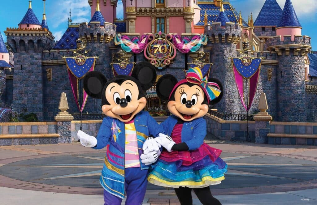 Disney teases Mickey and Minnie's colorful outfits for the 70th Anniversary Celebration in Disneyland and displayed behind them are all the 70th decorations draped over Sleeping Beauty castle.