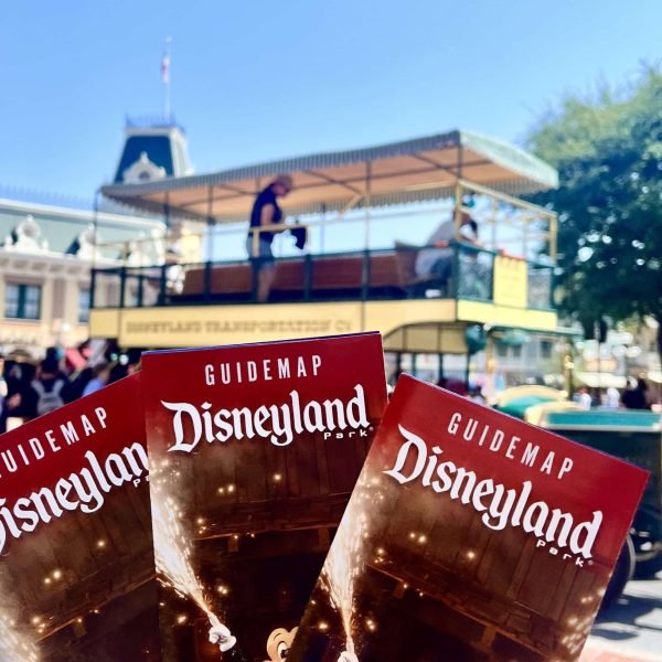 3 Disneyland Park Guide maps and a double decker trolley on Mainstreet U.S.A. in Disneyland Park on a clear blue sky day